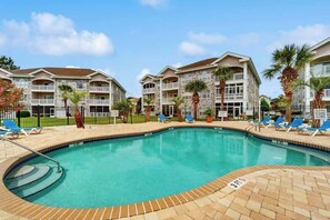 A swimming pool with lounge chairs and a stone building with balconies. - Wild Iris Unit 303 Condo (Myrtle Beach)
