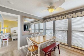 A dining area with a wooden table, white chairs, and a red bench. There is a ceiling fan above the table. - Ocean Bridge 2-C5 Sunrise Shore (Myrtle Beach)