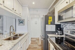 A kitchen with white cabinets, a stainless steel refrigerator, a stove, and a sink. - Ocean Bridge 2-C5 Sunrise Shore (Myrtle Beach)