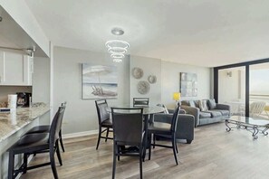 Ein modernes Wohnzimmer mit Essbereich, einem großen Fenster und einer Küche mit Marmorarbeitsplatte.