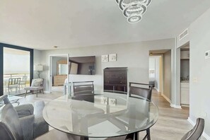 Un espace de salle à manger moderne, avec une table et des chaises en verre, un lustre et une vue sur l’extérieur.