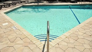 Piscina com escada de metal e deck revestido de azulejos.
