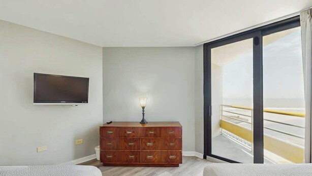 Quarto de hotel com cama, cômoda, televisão e varanda com guarda-corrimão.