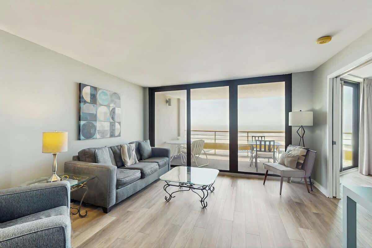 A modern living room with a sofa, a coffee table, and a balcony with a view.