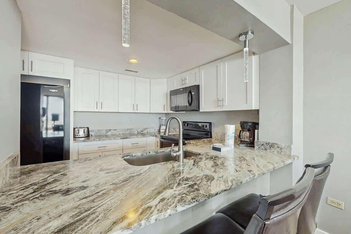 A modern kitchen with white cabinets, a granite countertop, a stainless steel sink, and a black refrigerator.