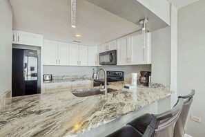 Une cuisine moderne avec des meubles blancs, un plan de travail en granit, un évier en acier inoxydable et un réfrigérateur noir.
