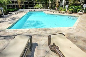 Ein rechteckiger Pool mit Fliesenrand, umgeben von Liegestühlen und Picknicktischen.