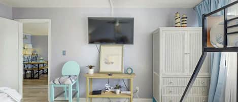 A bedroom with a bed, a TV mounted on the wall, a small table with a chair, and a wardrobe.