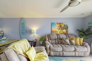 A living room with a sofa, armchair, and a surfboard decoration. - Holiday Towers Unit 301 (Myrtle Beach)