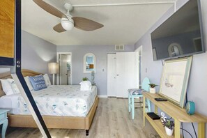 A bedroom with a bed, a desk, a chair, a ceiling fan, and a TV mounted on the wall. - Holiday Towers Unit 301 (Myrtle Beach)