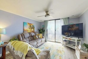 A living room with a sofa, a television, and a ceiling fan. - Holiday Towers Unit 301 (Myrtle Beach)