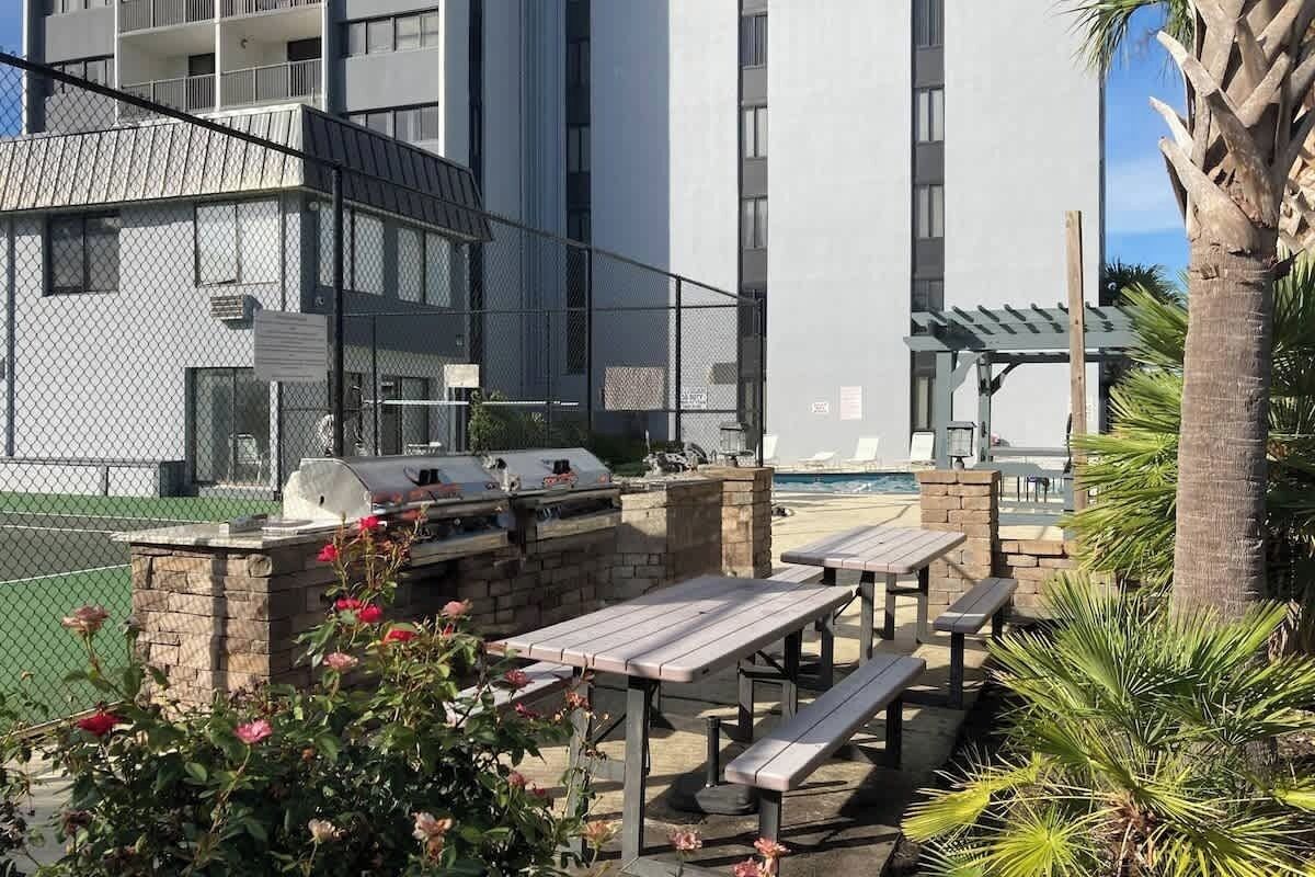 Eine Terrasse im Freien mit Grillanlagen, Picknicktischen und einem Pool im Hintergrund.