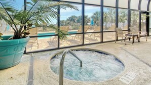 An indoor pool area with a hot tub, lounge chairs, and a large window offering a view of palm trees. - Meridian Plaza Unit 208 (Myrtle Beach)