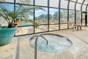 Ein Poolbereich im Innenbereich mit Whirlpool, Liegestühlen und einem großen Fenster mit Blick auf Palmen.
