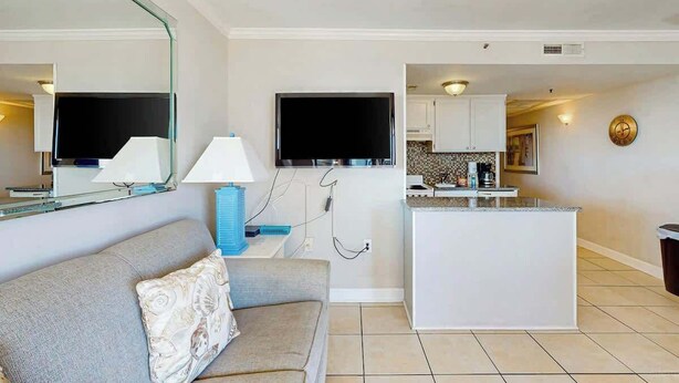 A modern living room with a sofa, a television, and a kitchen area with a counter and cabinets. - Meridian Plaza Unit 208 (Myrtle Beach)