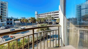 A balcony with a view of a parking garage, a building with a sign, and a clear blue sky. - Meridian Plaza Unit 208 (Myrtle Beach)