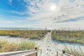 Ein Strand mit einem hölzernen Promenadenweg, der zum Wasser führt, umgeben von hohem Gras.