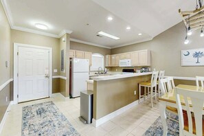 Una cocina con una isla central, armarios blancos, un refrigerador y un microondas.