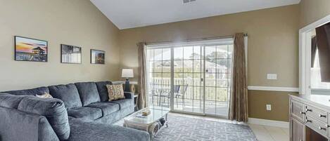 A living room with a grey sectional sofa, a coffee table, and a large window with curtains.
