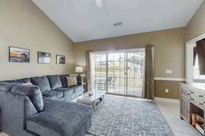 A living room with a grey sectional sofa, a coffee table, and a large window with curtains. - Myrtlewood Golf & Beach Retreat (Myrtle Beach)