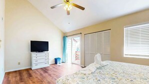 A bedroom with a bed, a television on a stand, a ceiling fan, and a sliding door leading to an outdoor area. - Brandywine South Unit 4G (Myrtle Beach)