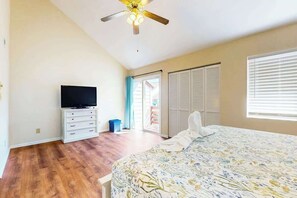 Ein Schlafzimmer mit einem Bett, einem Fernseher auf einem Schrank, einem Deckenventilator und einer Schiebetür, die zu einem Außenbereich führt.
