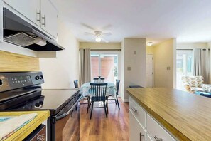 A compact kitchen with a gas stove, a ceiling fan, and a dining area with a table and chairs. - Brandywine South Unit 4G (Myrtle Beach)
