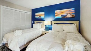 Habitación de hotel con dos camas, un armario y dos cuadros en la pared.