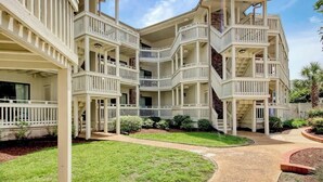 Un edificio de varios pisos con balcones, un paseo cubierto y un jardín ajardinado.
