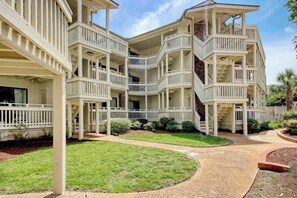 A multi-story building with balconies, a covered walkway, and a landscaped garden. - Chelsea House Villas 112 (Myrtle Beach)