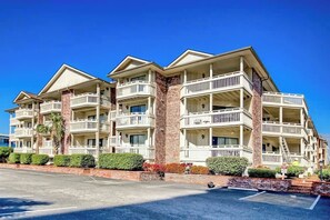 A multi-story hotel with balconies, a brick facade, and a parking lot. - Chelsea House Villas 112 (Myrtle Beach)