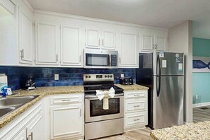 A modern kitchen with white cabinets, stainless steel appliances, and a granite countertop. - Chelsea House Villas 112 (Myrtle Beach)
