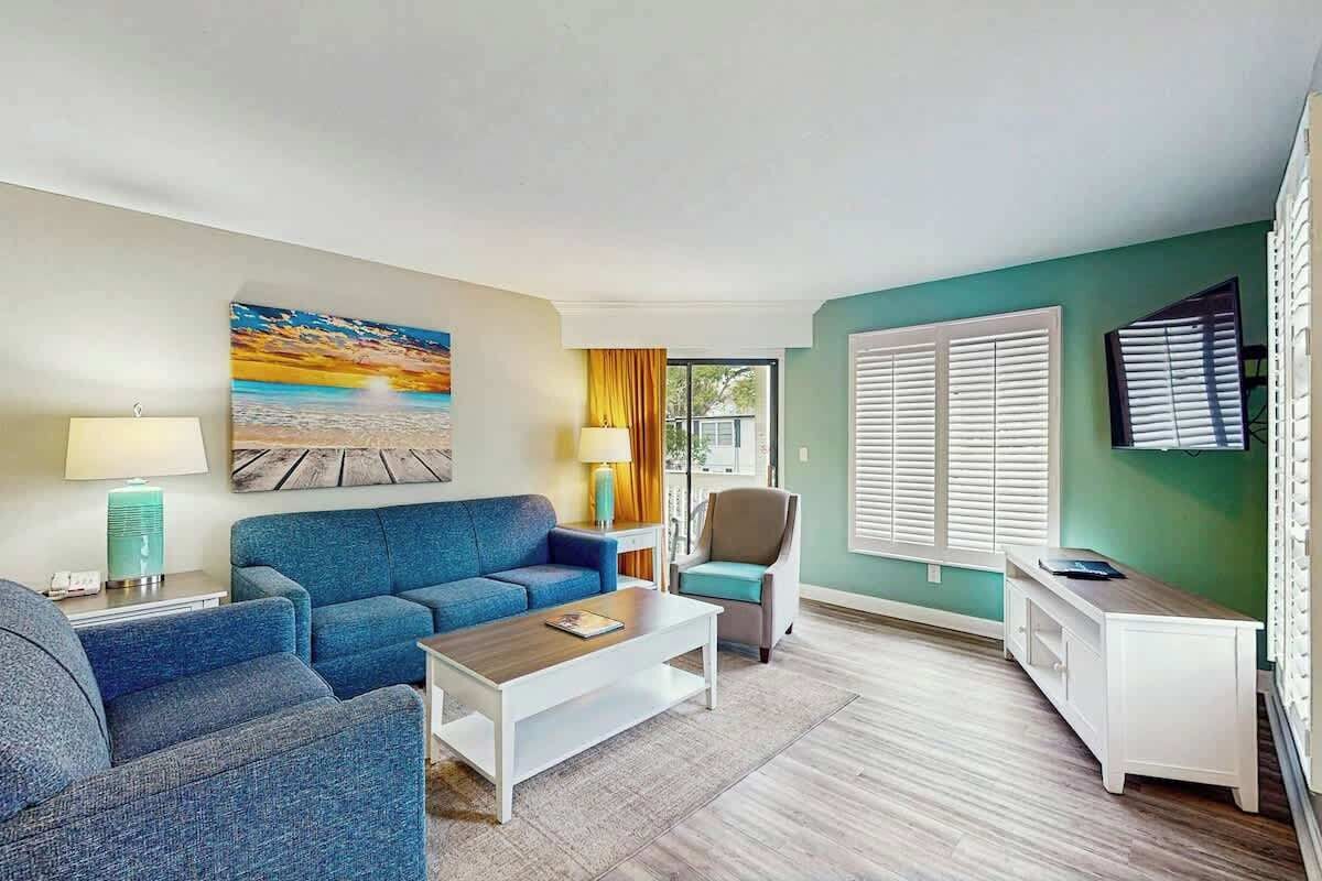A living room with a blue sofa, a coffee table, and a painting of a sunset.