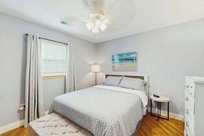 A bedroom with a bed, bedside table, lamp, and a painting on the wall. - Beach House Hideaway (North Myrtle Beach)