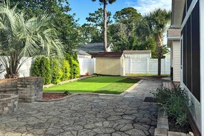 A backyard with a stone patio, a well-maintained lawn, and a white fence. - Beach House Hideaway (North Myrtle Beach)