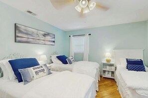 A bedroom with two beds, a ceiling fan, a window with blinds, and a wall-mounted artwork. - Beach House Hideaway (North Myrtle Beach)