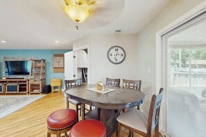 A dining area with a round table, four chairs, a clock on the wall, and a television in the background. - Beach House Hideaway (North Myrtle Beach)