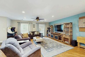 A living room with a sofa, coffee table, TV stand, and a ceiling fan. - Beach House Hideaway (North Myrtle Beach)
