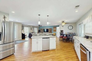 A modern kitchen with a central island, stainless steel appliances, and a dining area with chairs and a table. - Beach House Hideaway (North Myrtle Beach)