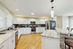A modern kitchen with white cabinets, a central island, and a stainless steel refrigerator. - Beach House Hideaway (North Myrtle Beach)