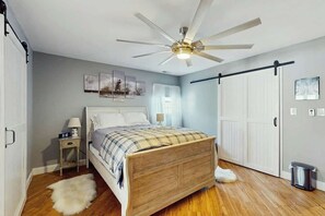 A bedroom with a wooden bed, a ceiling fan, a nightstand, a white door, and a wall-mounted light. - Beach House Hideaway (North Myrtle Beach)