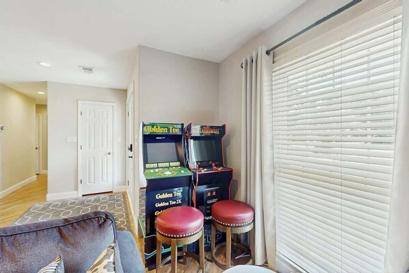 A room with a sofa, two stools, and two arcade machines. - Beach House Hideaway (North Myrtle Beach)