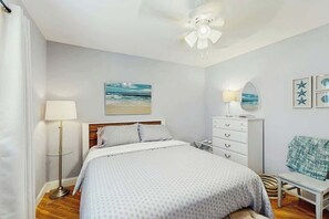 A bedroom with a bed, a bedside lamp, a dresser, a ceiling fan, and a beach-themed wall art. - Beach House Hideaway (North Myrtle Beach)