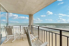 Ein Balkon mit Blick auf den Ozean, ein weißer Schaukelstuhl, ein kleiner Tisch und eine Glastür zum Strand.