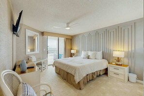 A hotel room with a bed, bedside tables, a desk, a chair, a ceiling fan, and a view of the outdoors. - Surfmaster by the Sea 208 (Murrells Inlet)