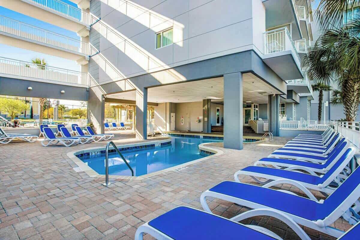 A pool area with lounge chairs, a swimming pool, and a building with balconies.