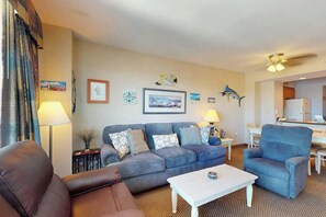 A living room with a sofa, armchair, and coffee table. There are wall decorations, a lamp, and a ceiling fan. - Harbourgate Unit 0620 (North Myrtle Beach)