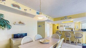 Un espace repas comprenant une longue table, des chaises et un ventilateur. Il y a également un coin cuisine avec un four à micro-ondes et des placards.