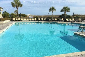 A clear blue pool with lounge chairs and palm trees, surrounded by a fence. - Ocean Creek Lodge IV - 2287 (Myrtle Beach)