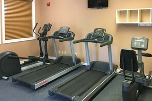 Drei Laufbänder in einem Fitnessstudio, darüber ein Fernseher und eine Wandablage mit Gegenständen.